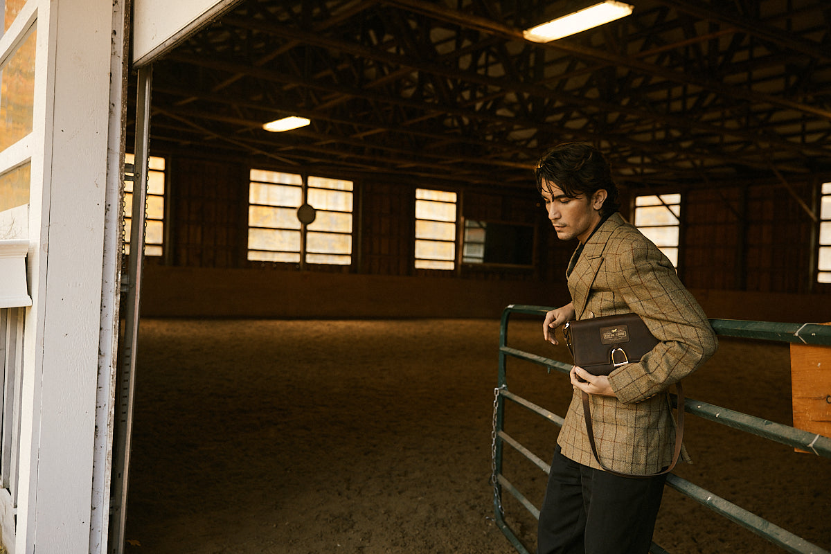 Person standing in a stable holding a black bag
