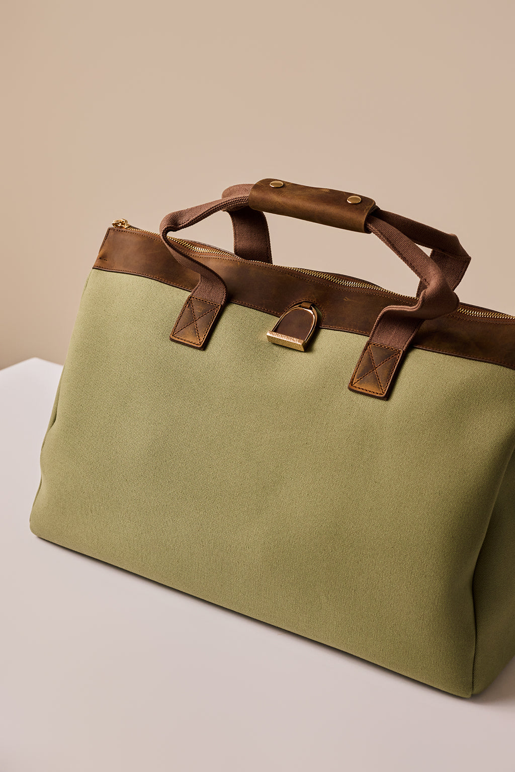 Green bag with brown leather handles on a beige background