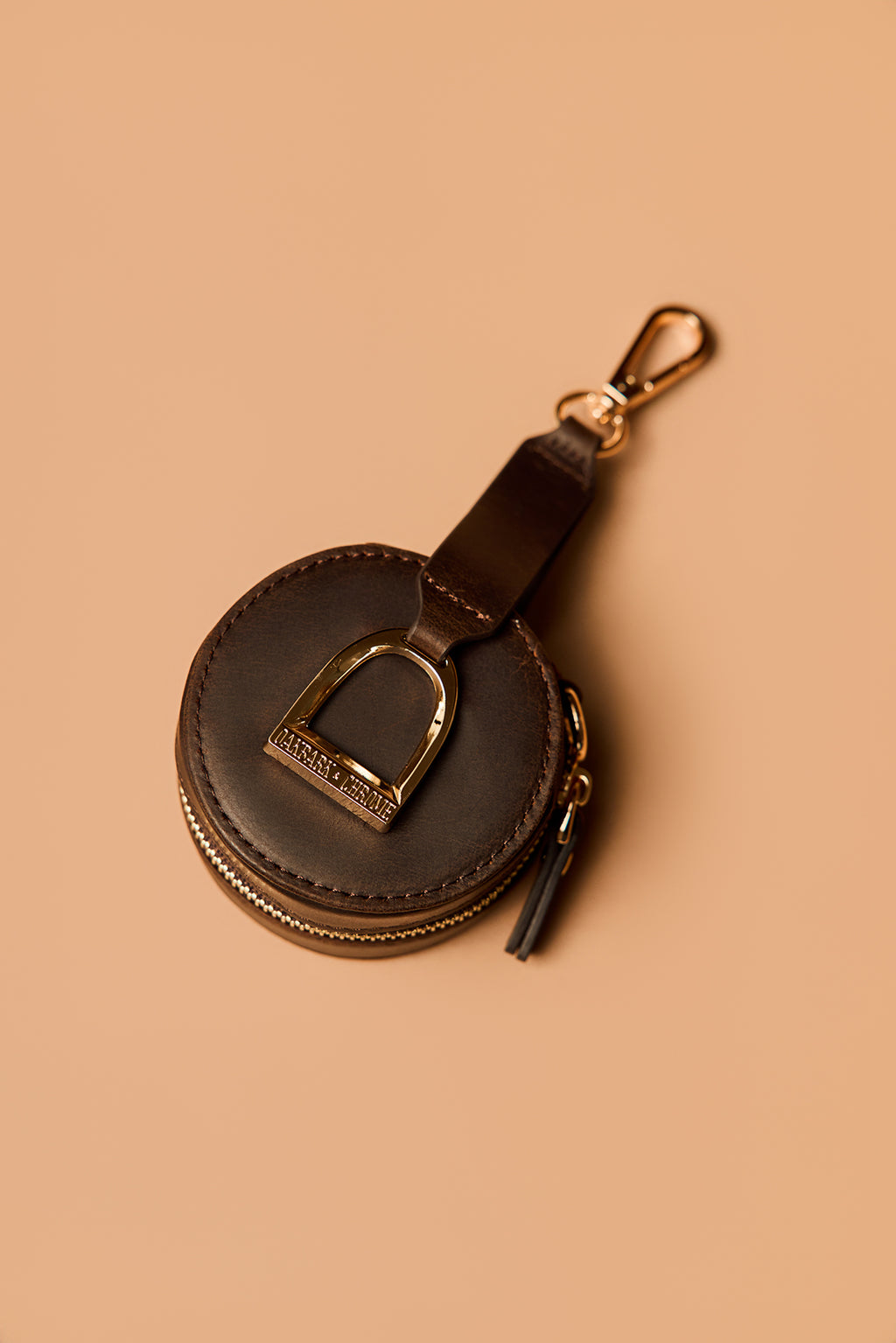 Brown leather keychain with gold accent on a beige background