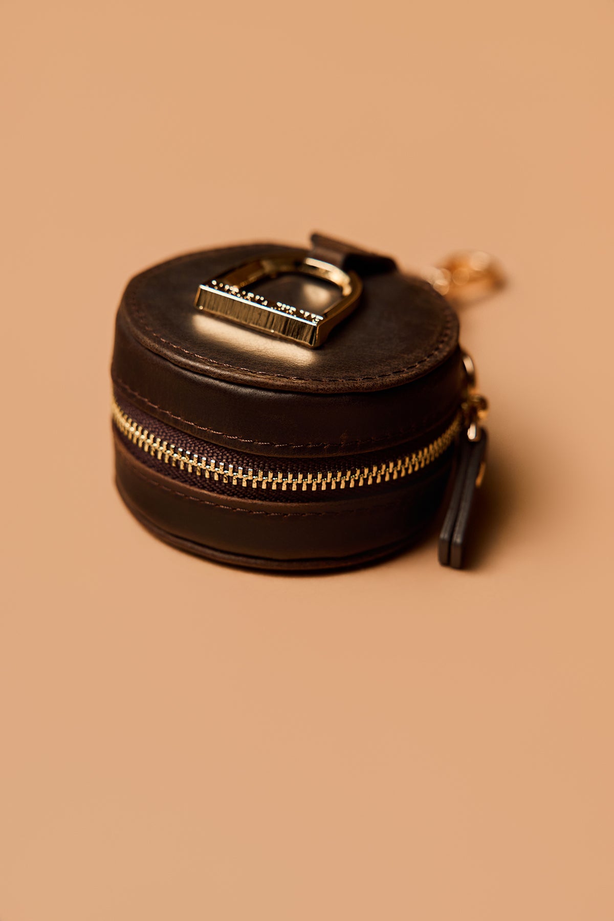 Round black leather pouch with gold zipper on a beige background