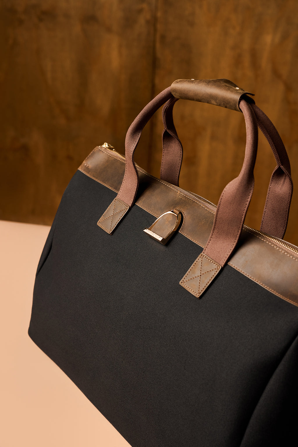 Black bag with brown leather handles on a beige surface