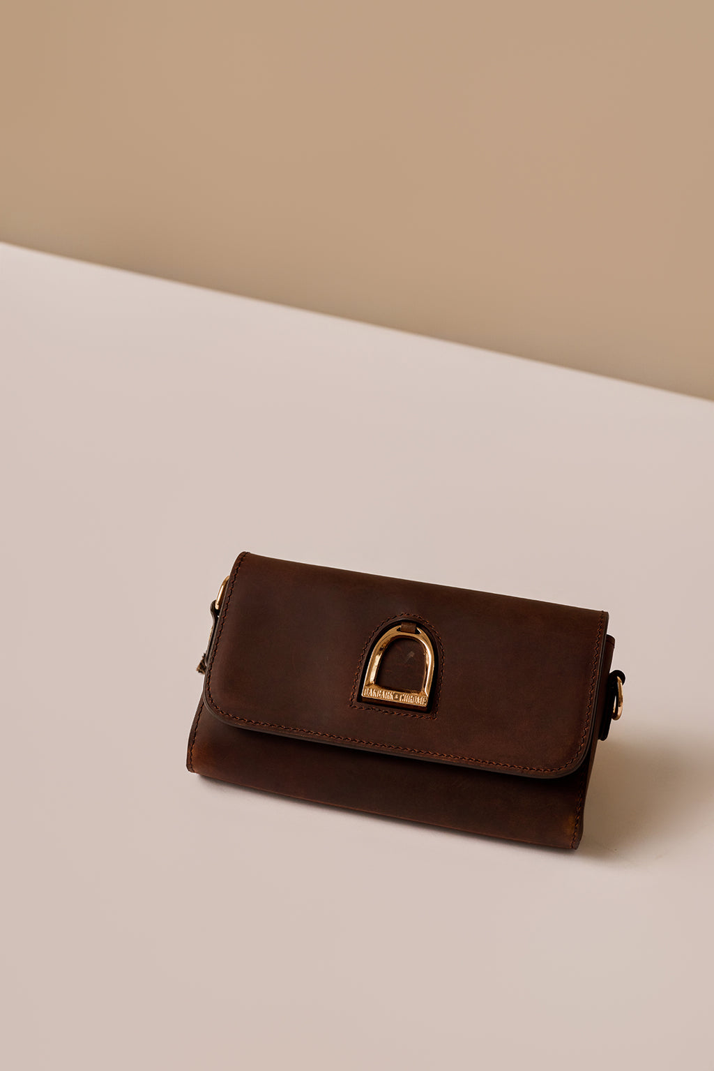 Brown leather clutch with gold buckle on a beige background
