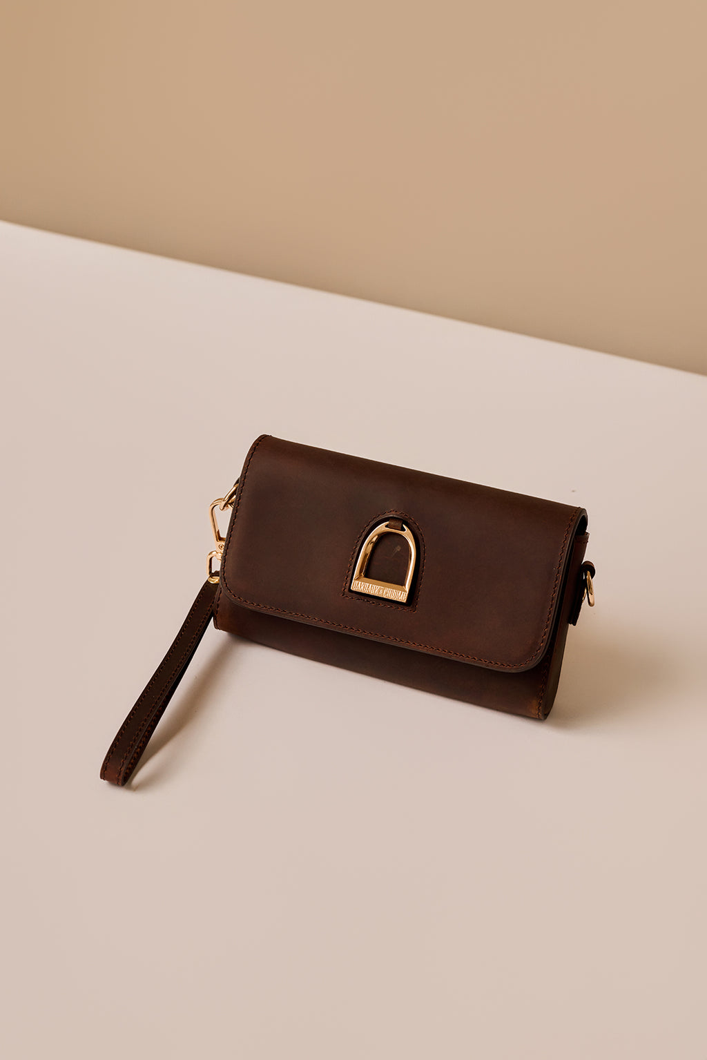 Brown leather clutch with gold clasp on a beige background