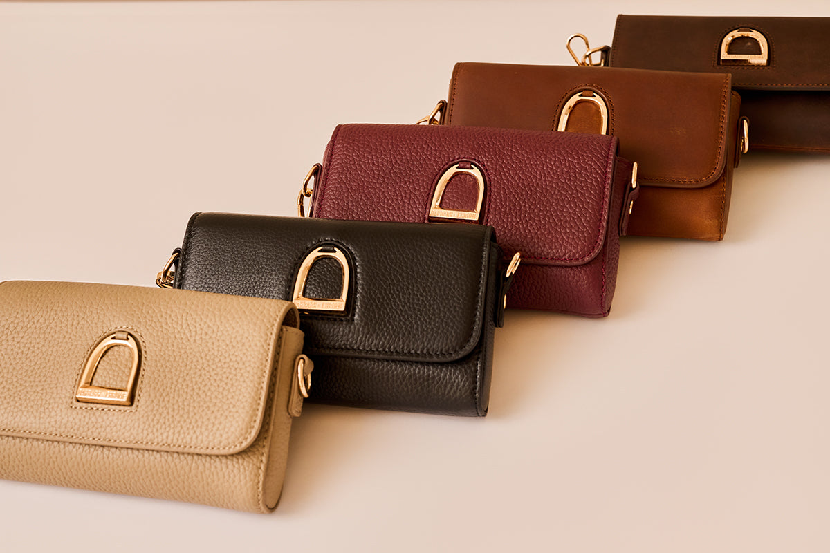 Row of leather handbags in various colors on a beige background