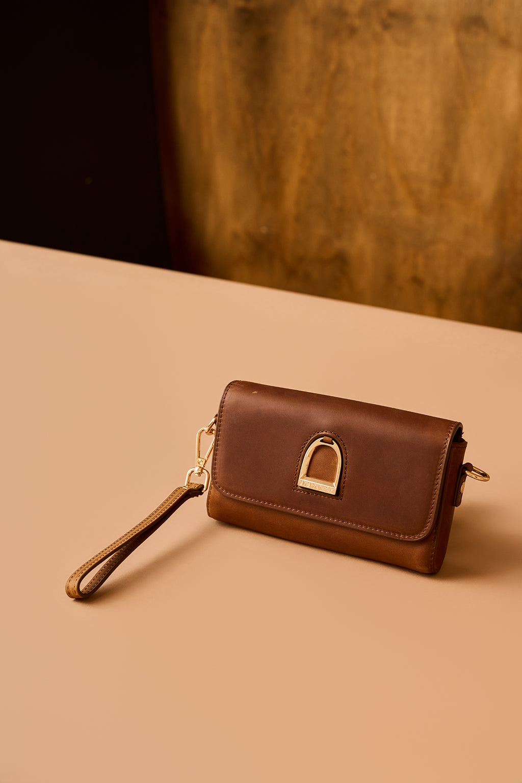 Brown leather wallet with a strap on a beige surface