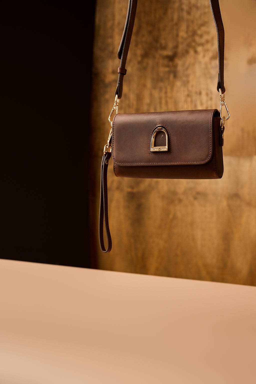 Brown leather handbag with a gold clasp on a reflective surface with a blurred background