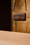 Brown leather handbag with a gold clasp on a reflective surface with a blurred background