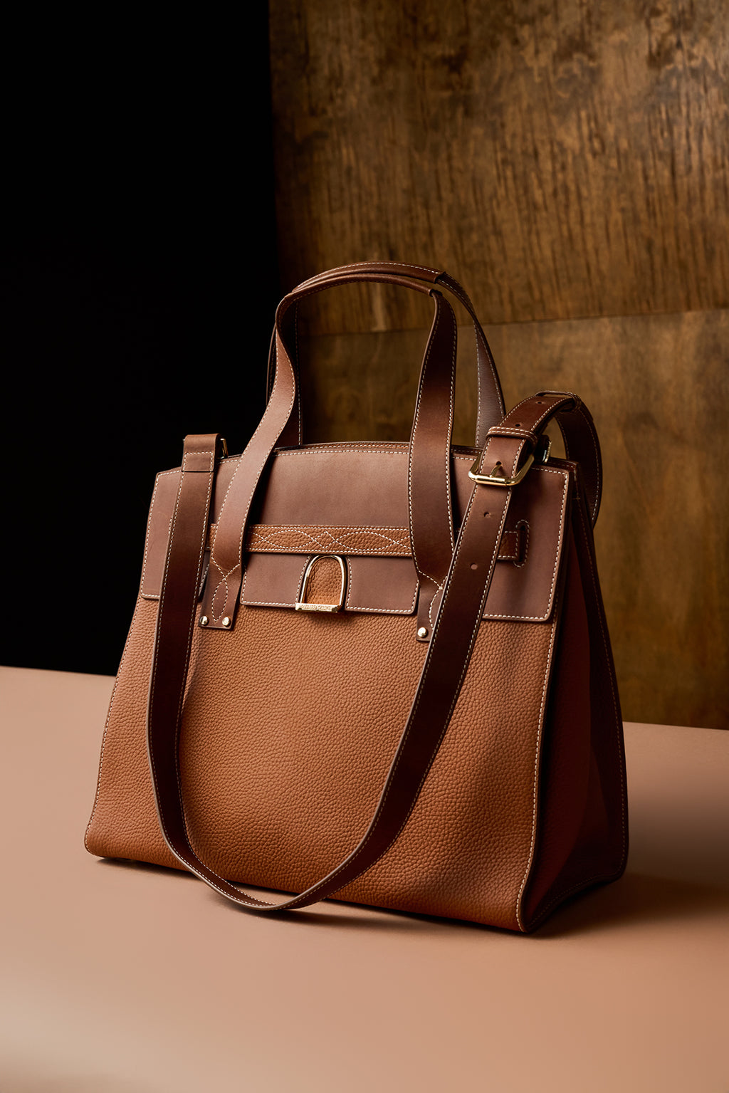 Brown leather handbag on a beige surface with a dark brown background