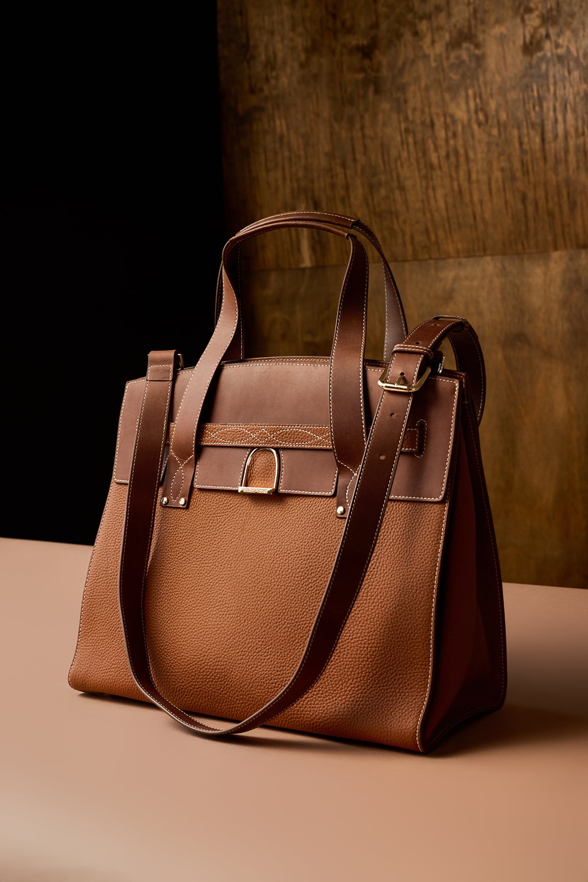 Brown leather handbag on a beige surface with a dark brown background
