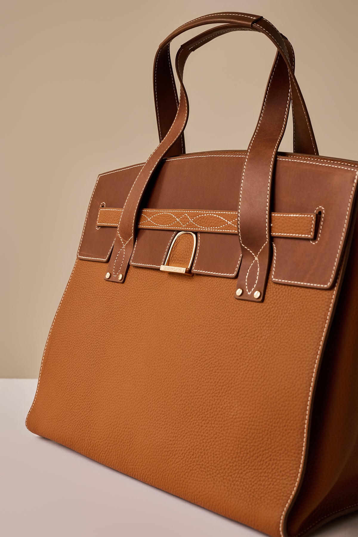Brown leather handbag with gold accents on a beige background