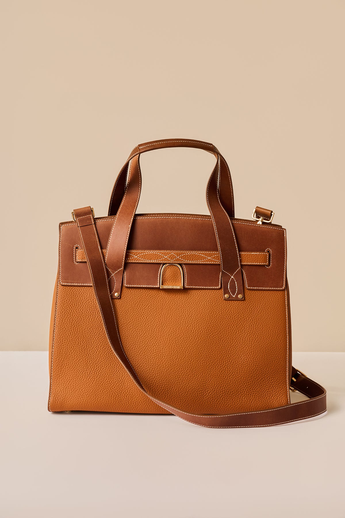 Brown leather handbag with a matching strap on a beige background