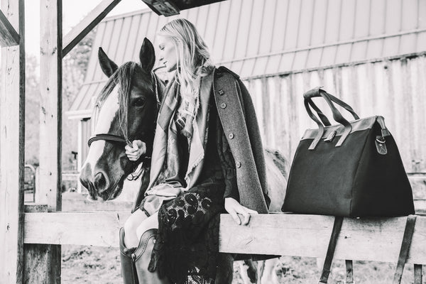 Woman with a horse and a black leather bag in an outdoor setting