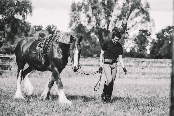 Man leading a horse in an open field with trees in the background