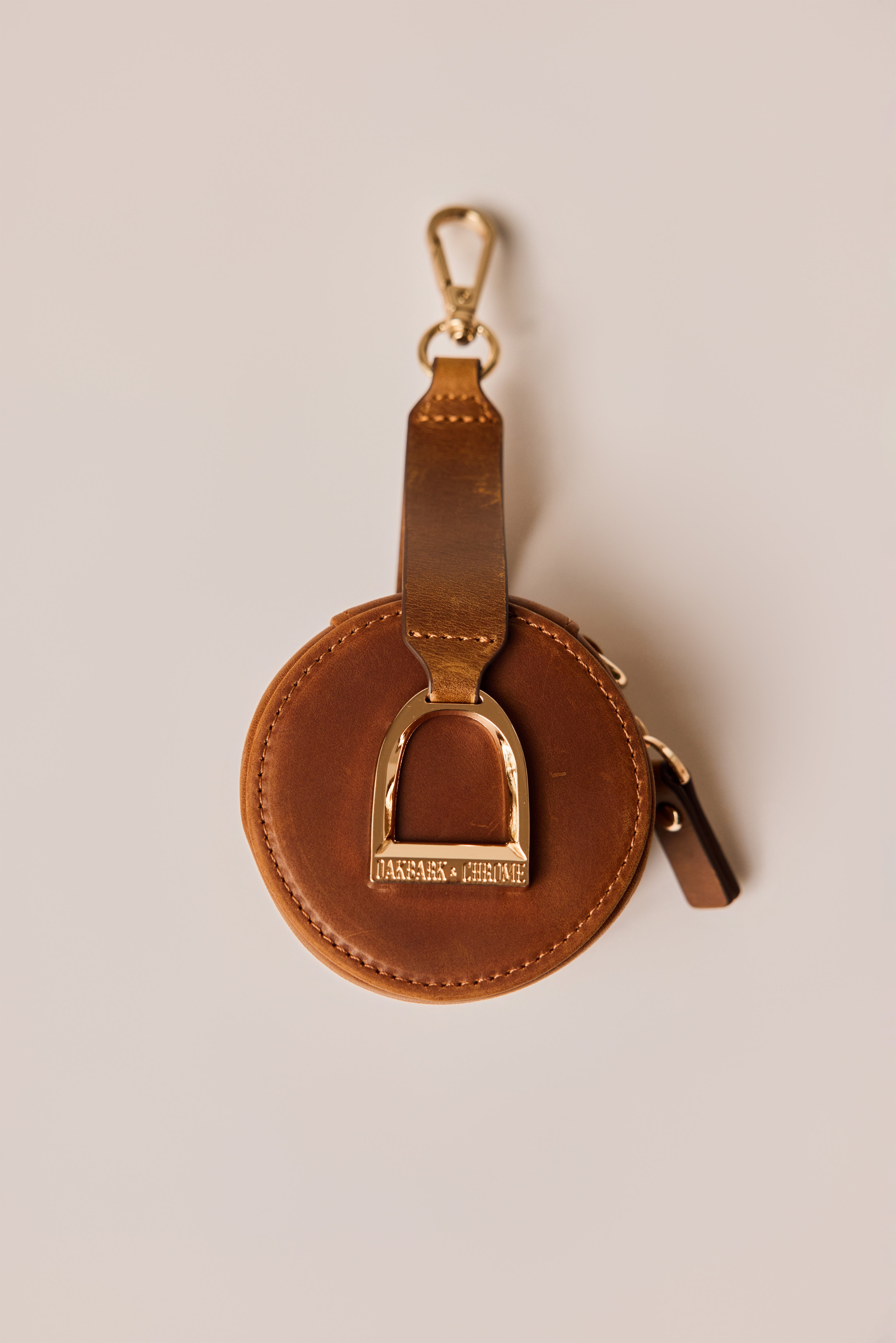 Brown leather keychain with gold horse stirrup on a beige background