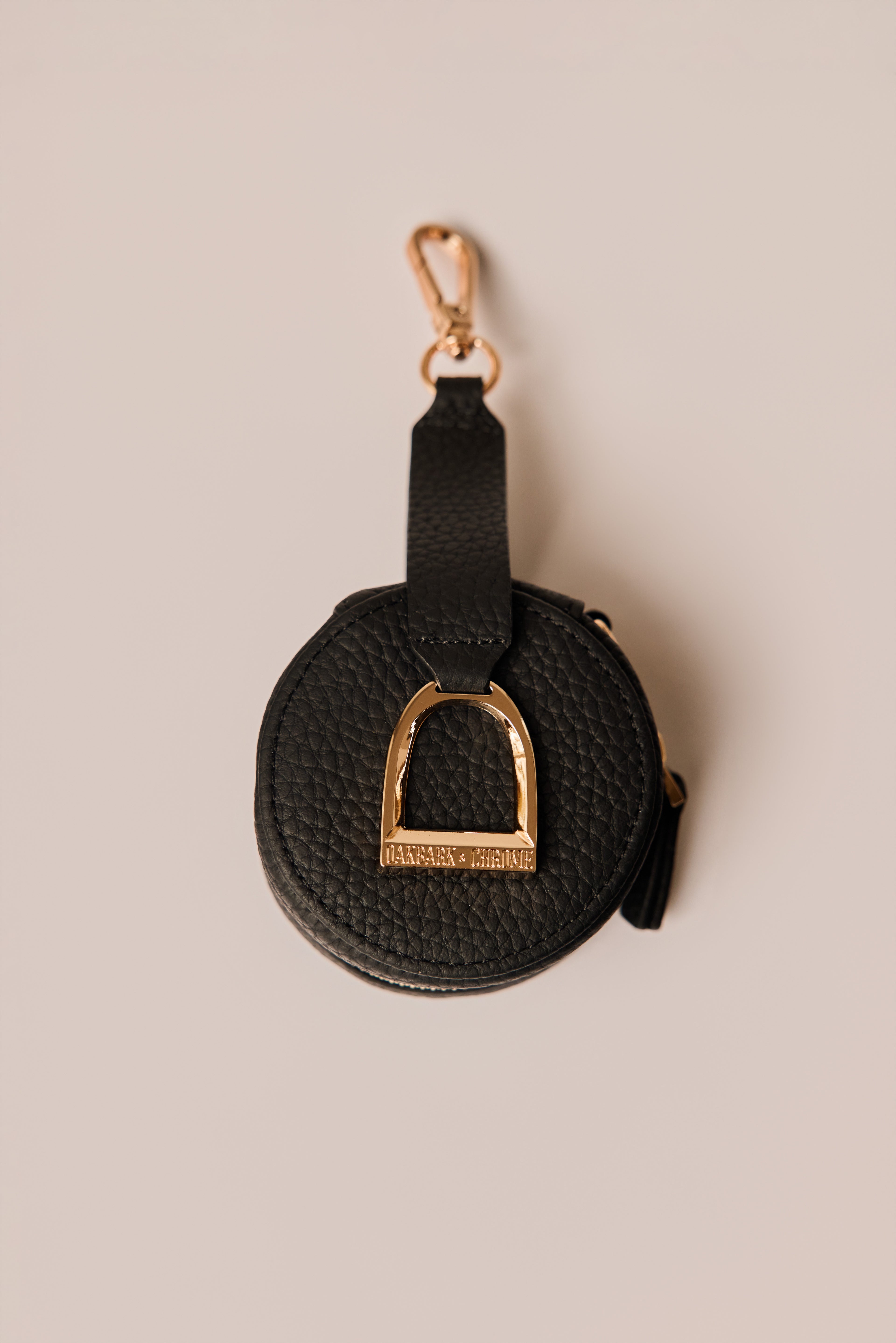 Black leather keychain with gold hardware on a beige background