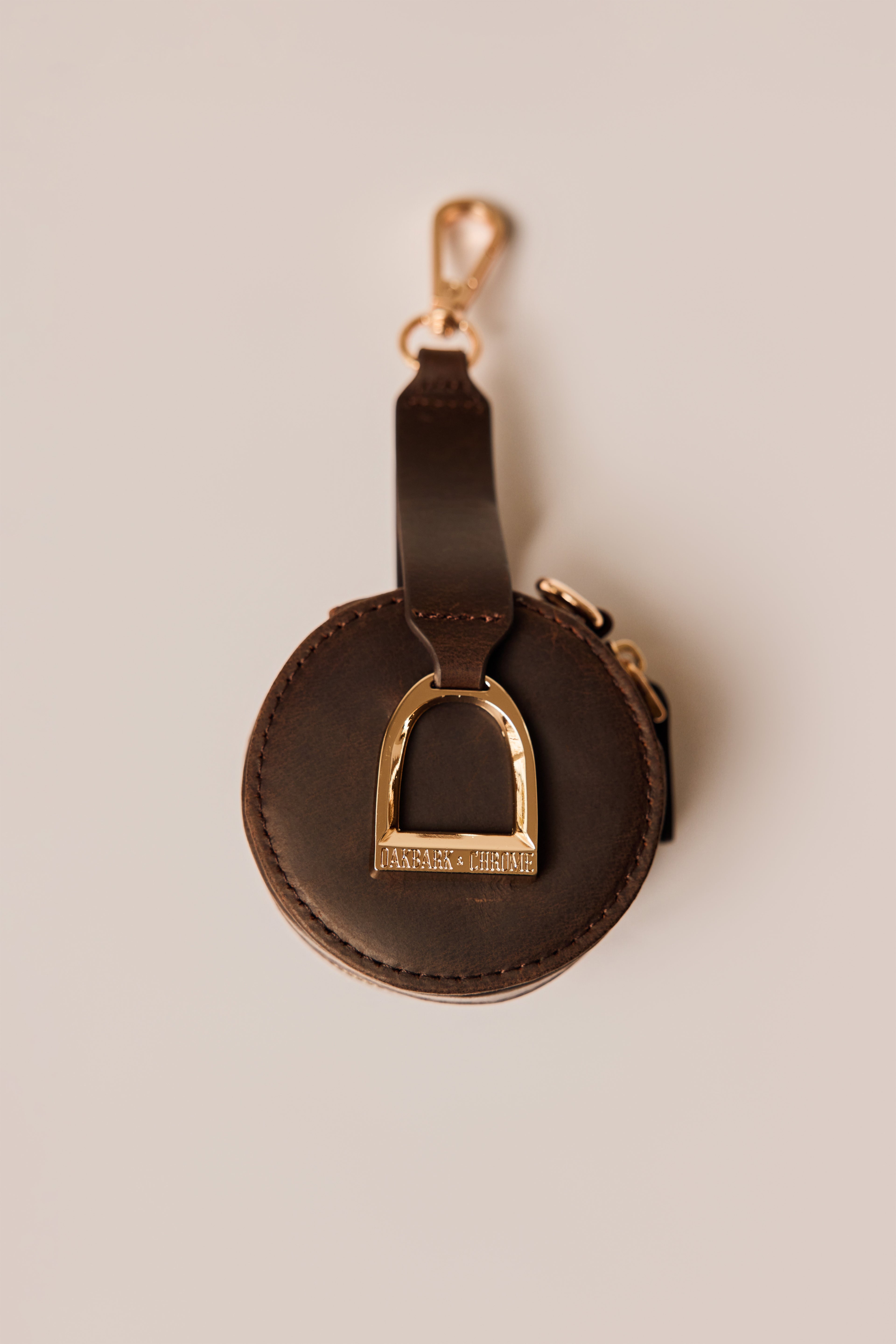 Brown leather keychain with gold horse stirrup charm on a beige background