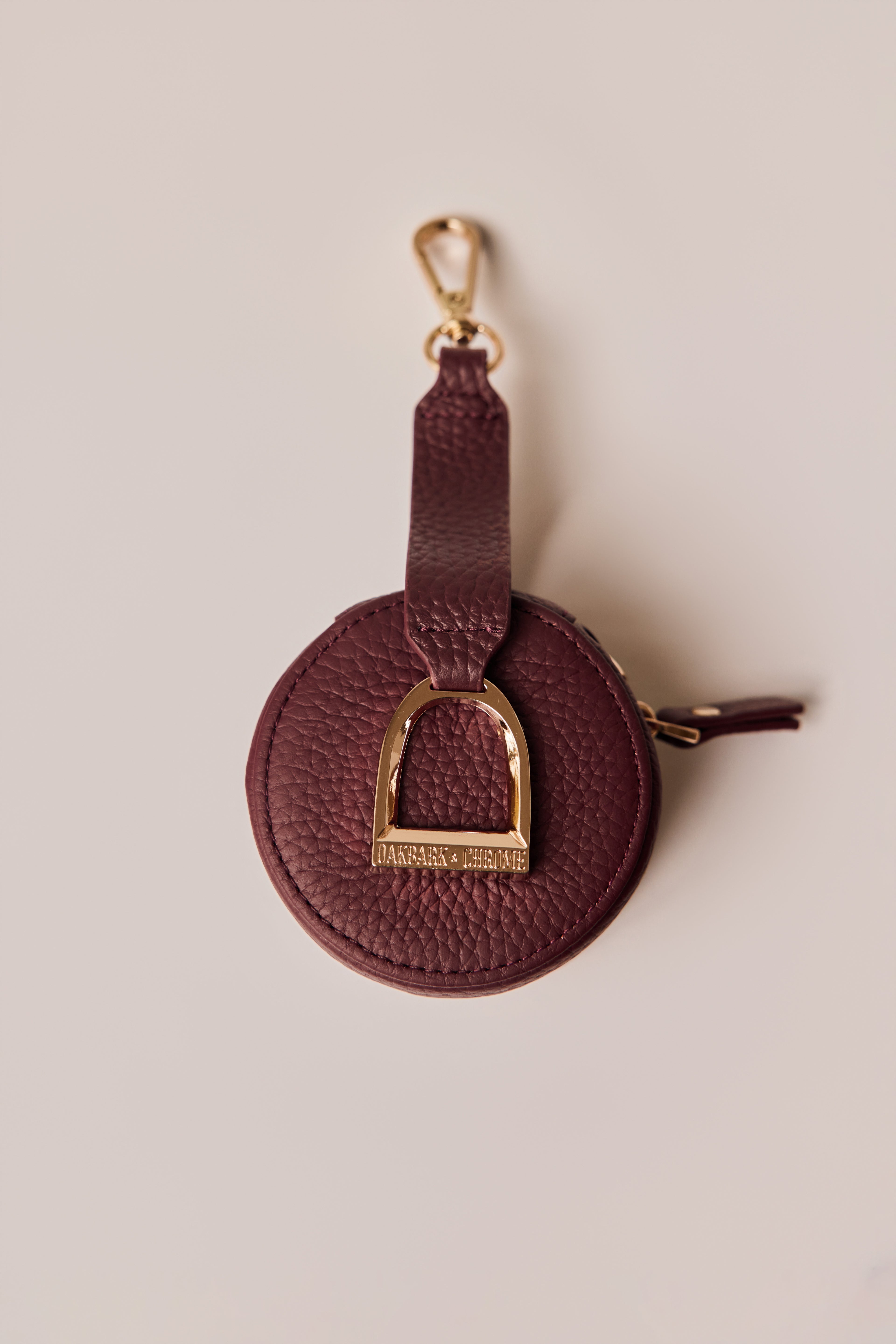 Wine leather keychain with gold horse stirrup on a beige background