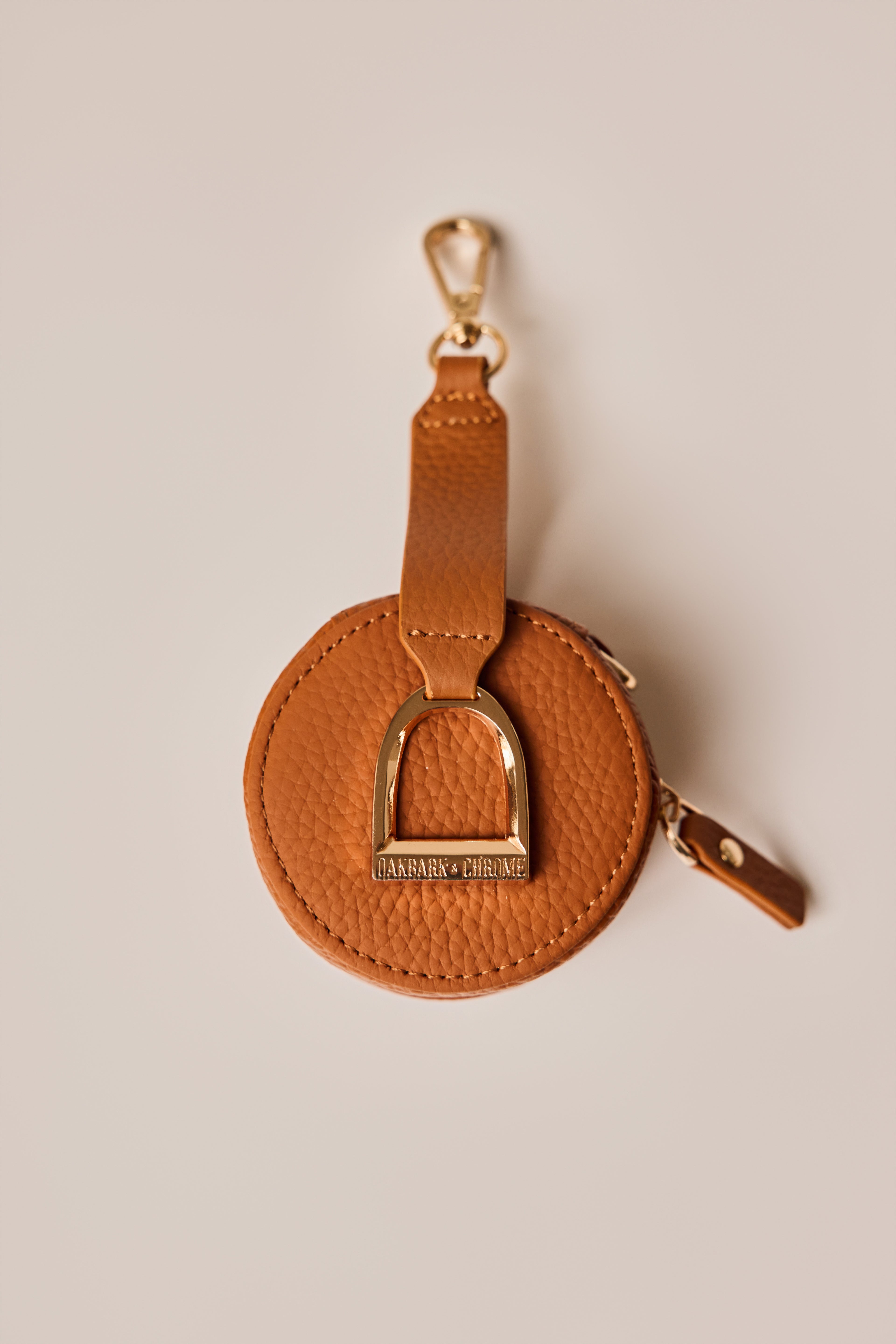 Brown leather keychain with gold accents on a beige background