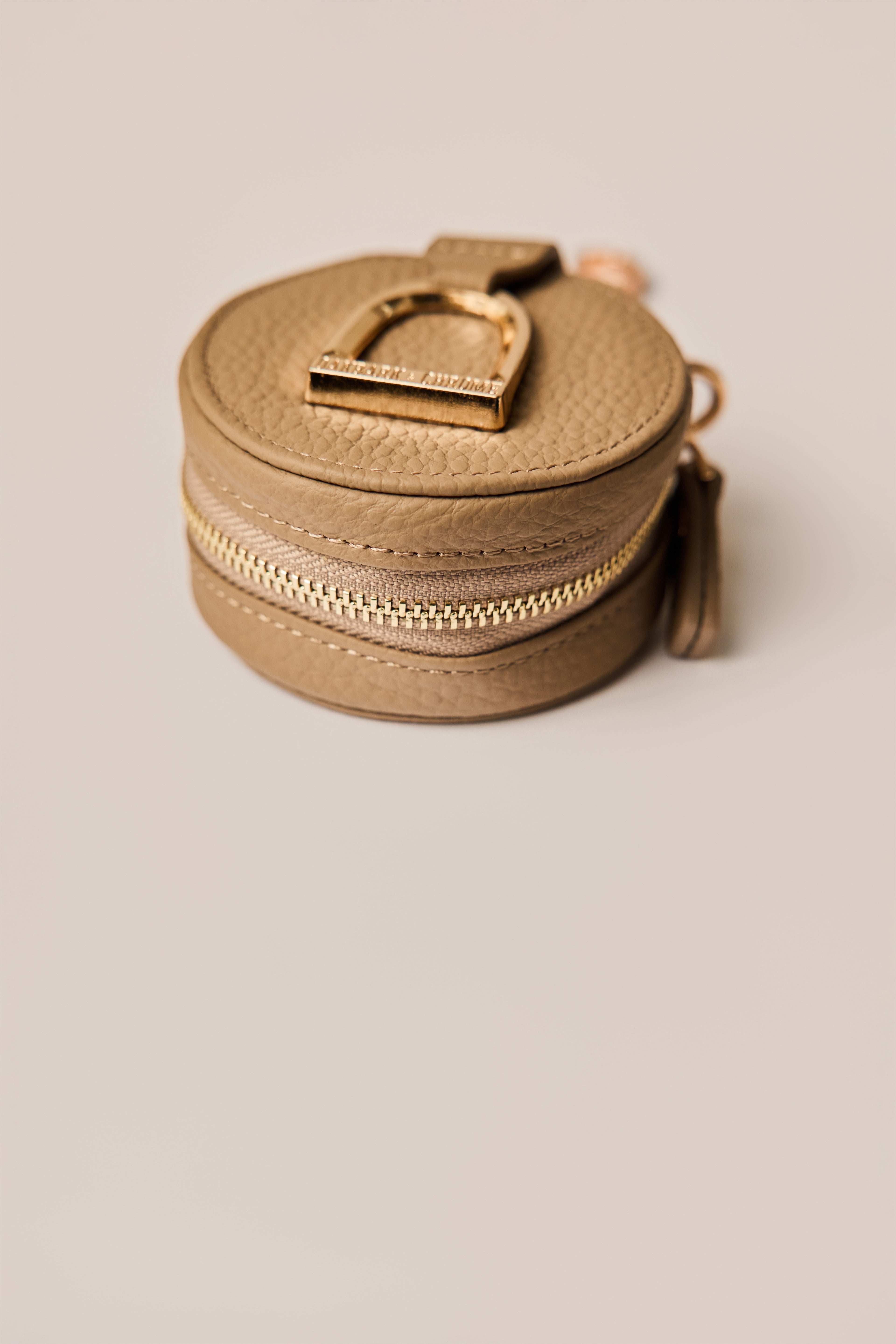 Round beige leather pouch with a gold zipper on a beige background
