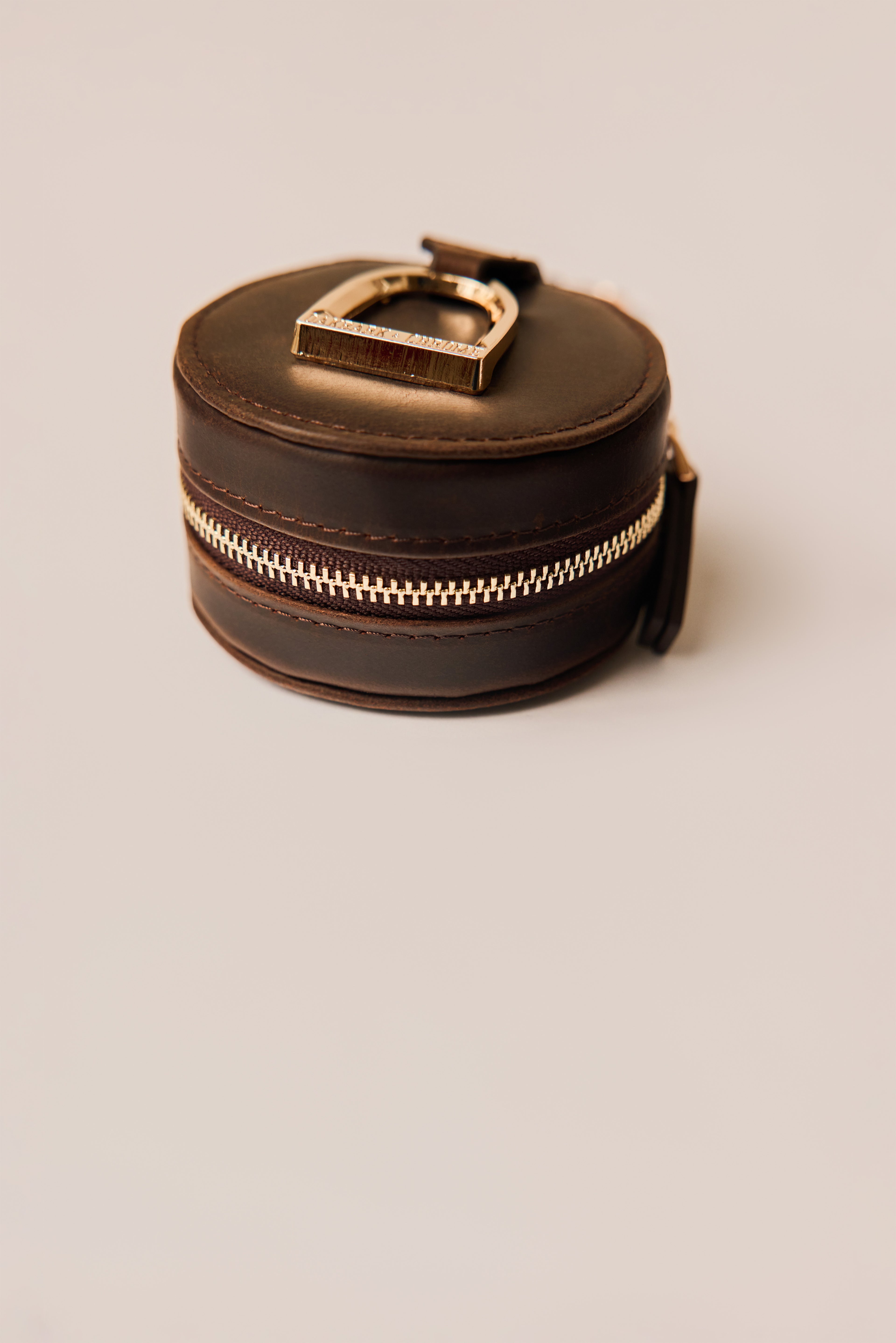 Round leather jewelry box with gold clasp on a beige background