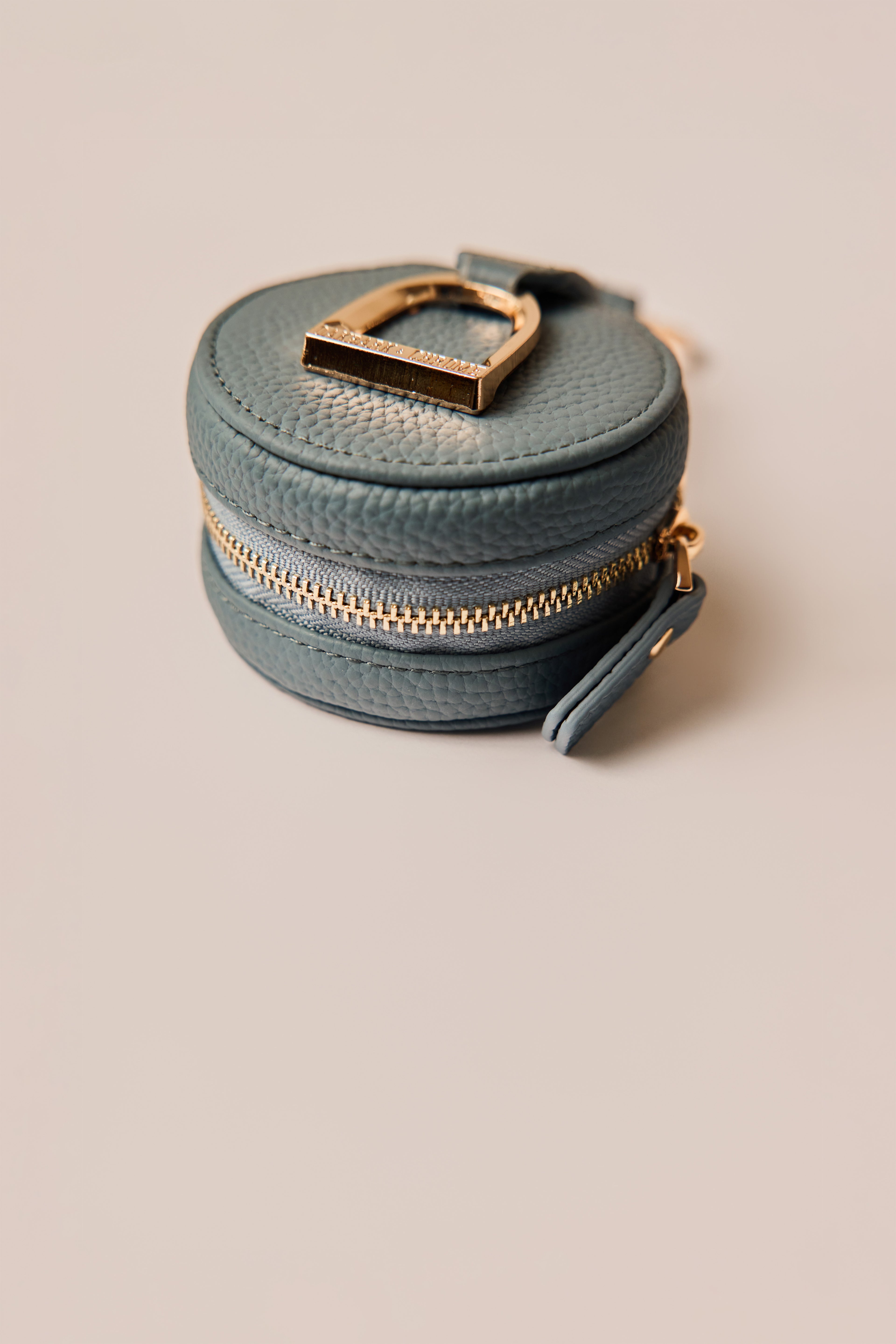 Round blue leather pouch with gold zipper and clasp on a beige background