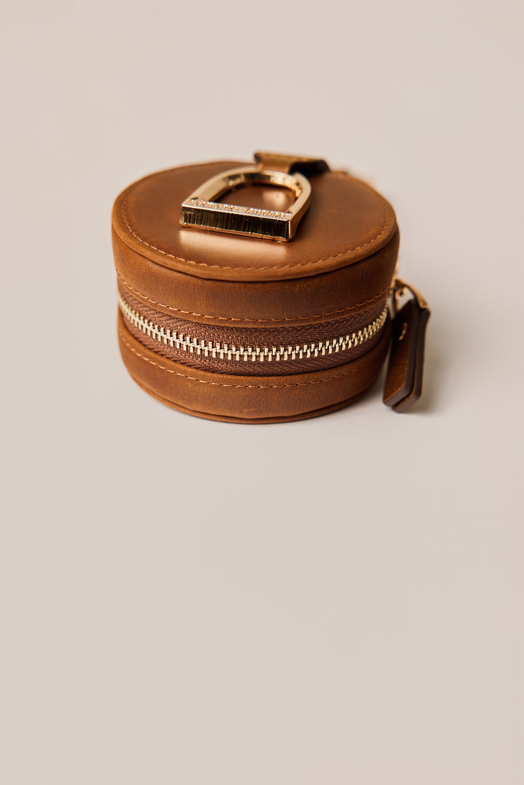 Brown leather keychain with gold horse stirrup on a beige background