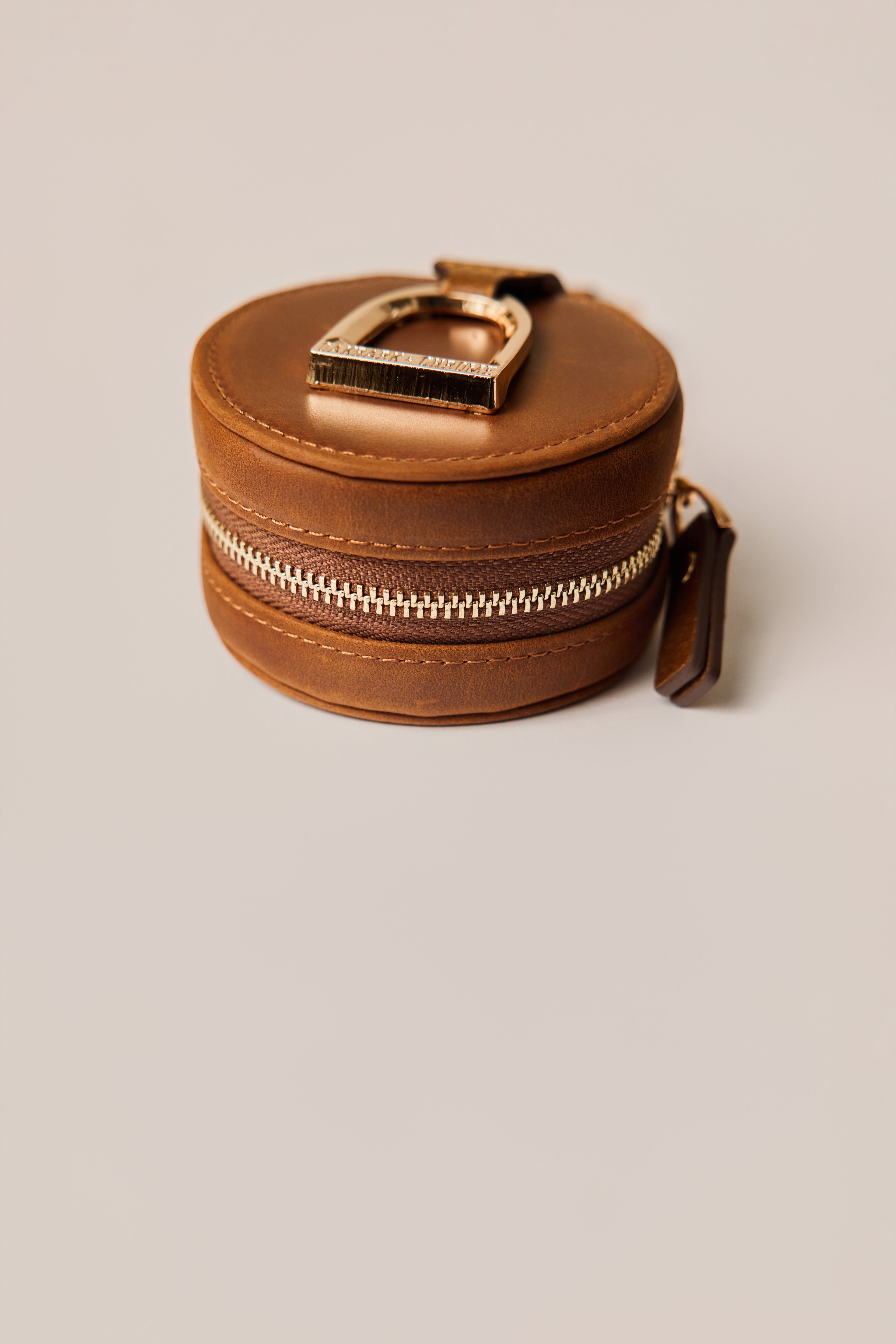 Brown leather keychain with gold horse stirrup on a beige background