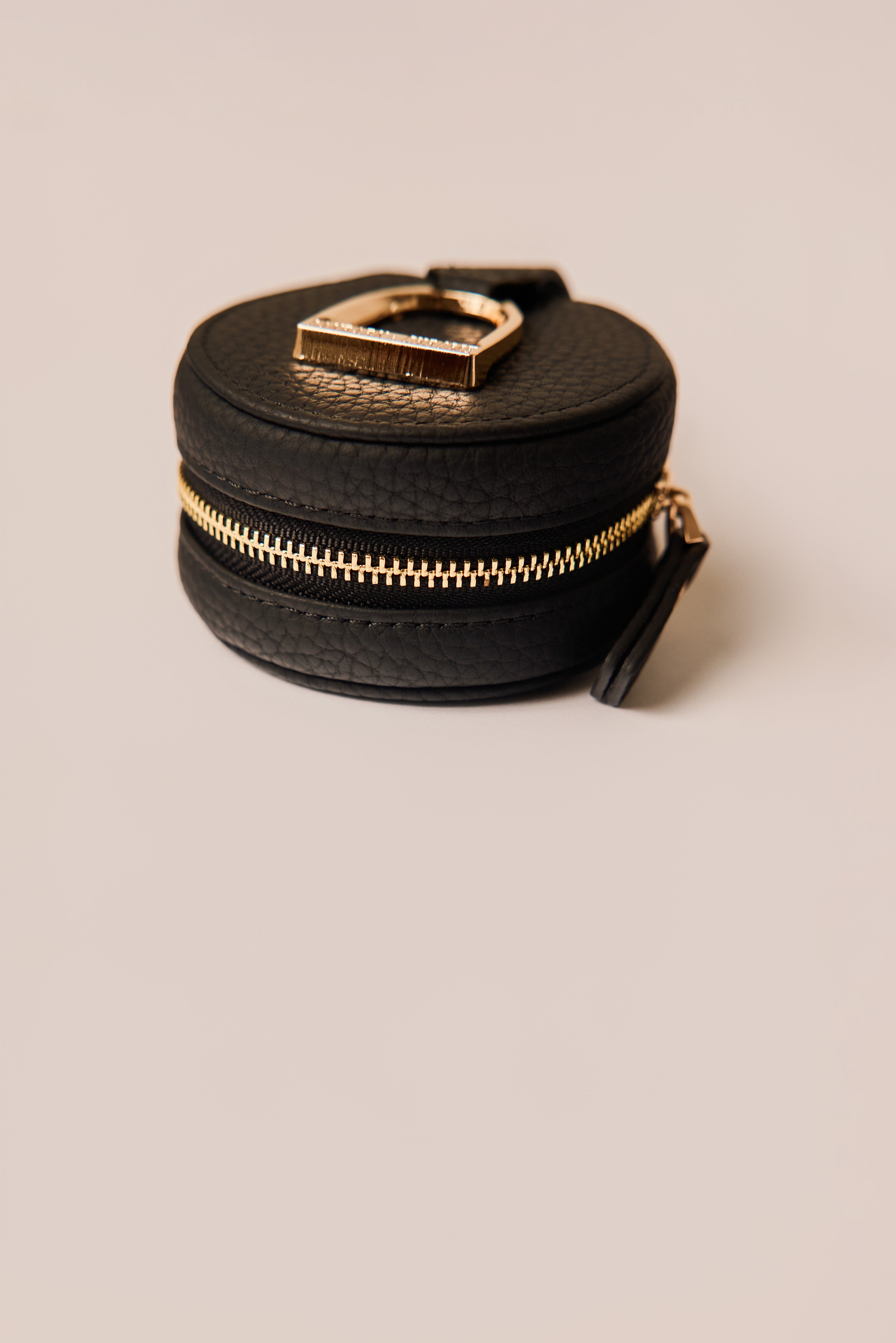 Black round jewelry box with gold zipper on a beige background