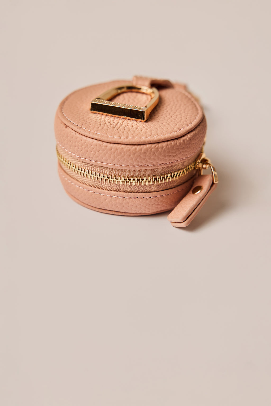 Pink round jewelry case with gold zipper and handle on a beige background
