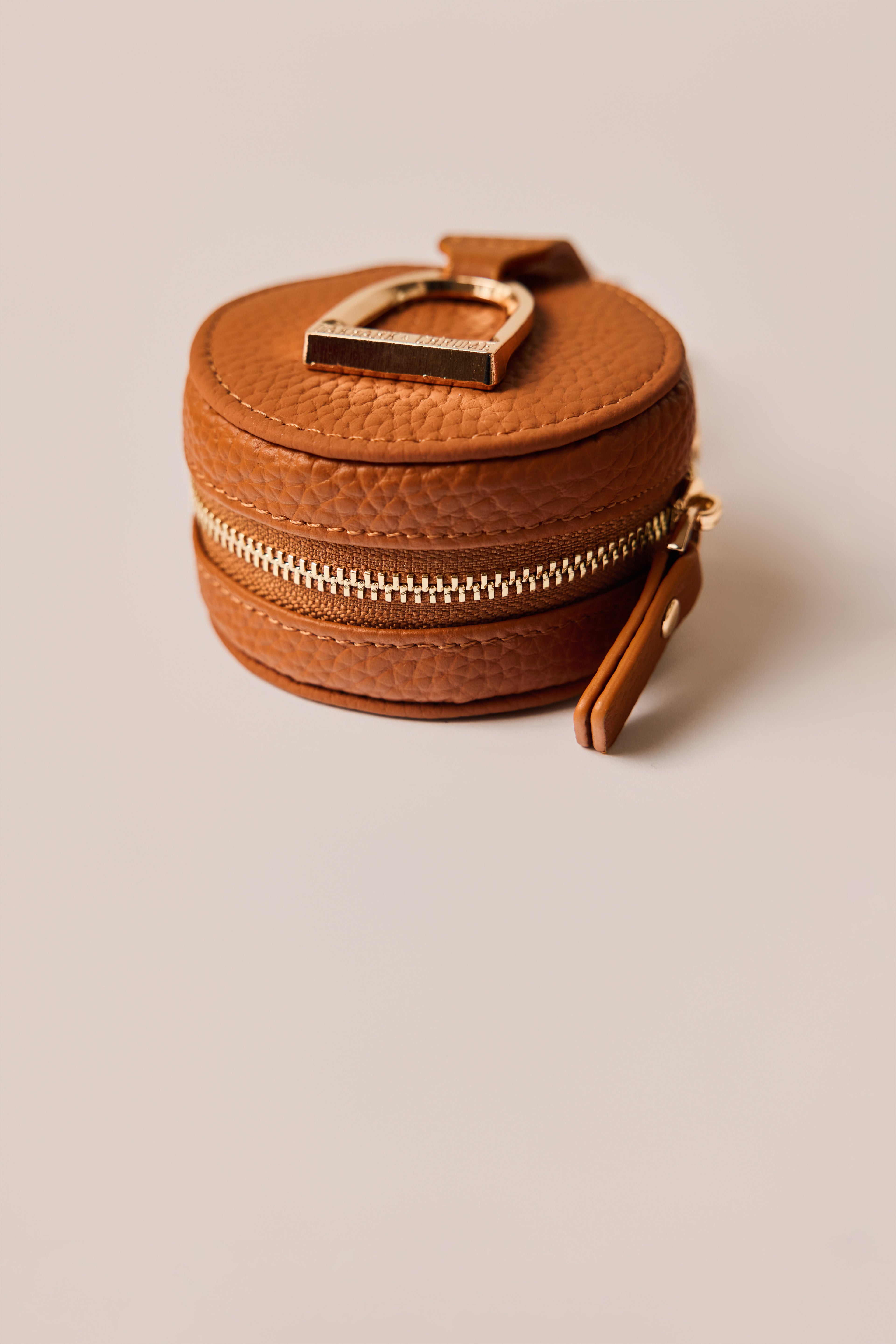Brown leather jewelry box with gold zipper and clasp on a beige background