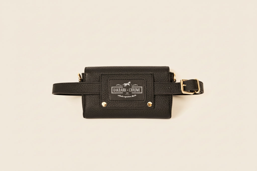 Black leather waist bag with gold accents on a beige background
