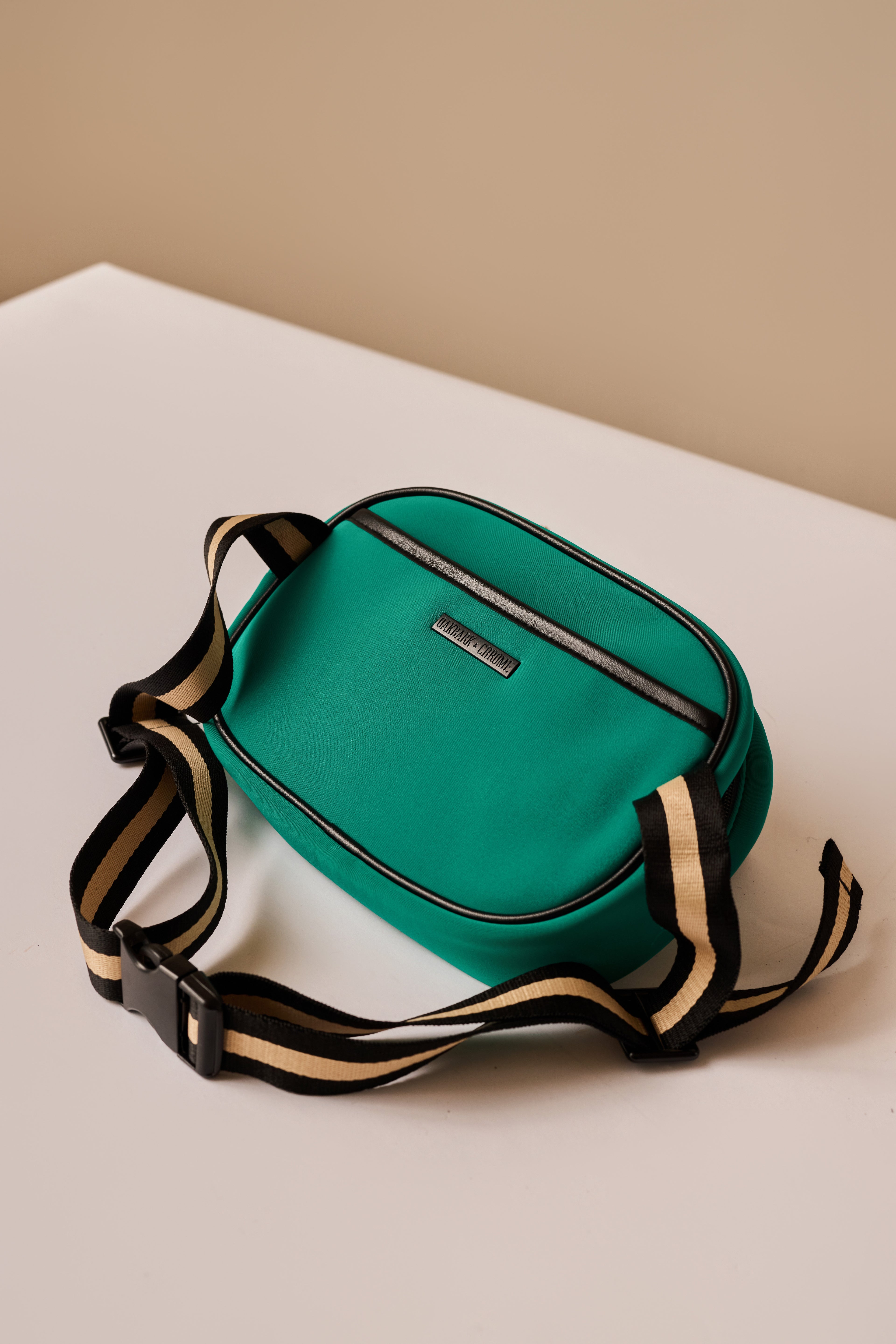 Green crossbody bag with a strap on a beige surface