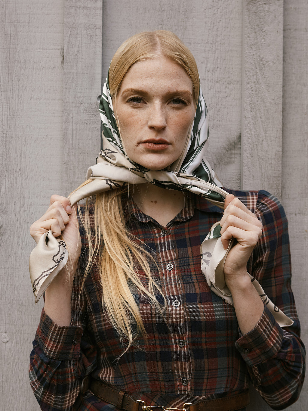 Woman wearing a patterned scarf and plaid shirt against a gray background