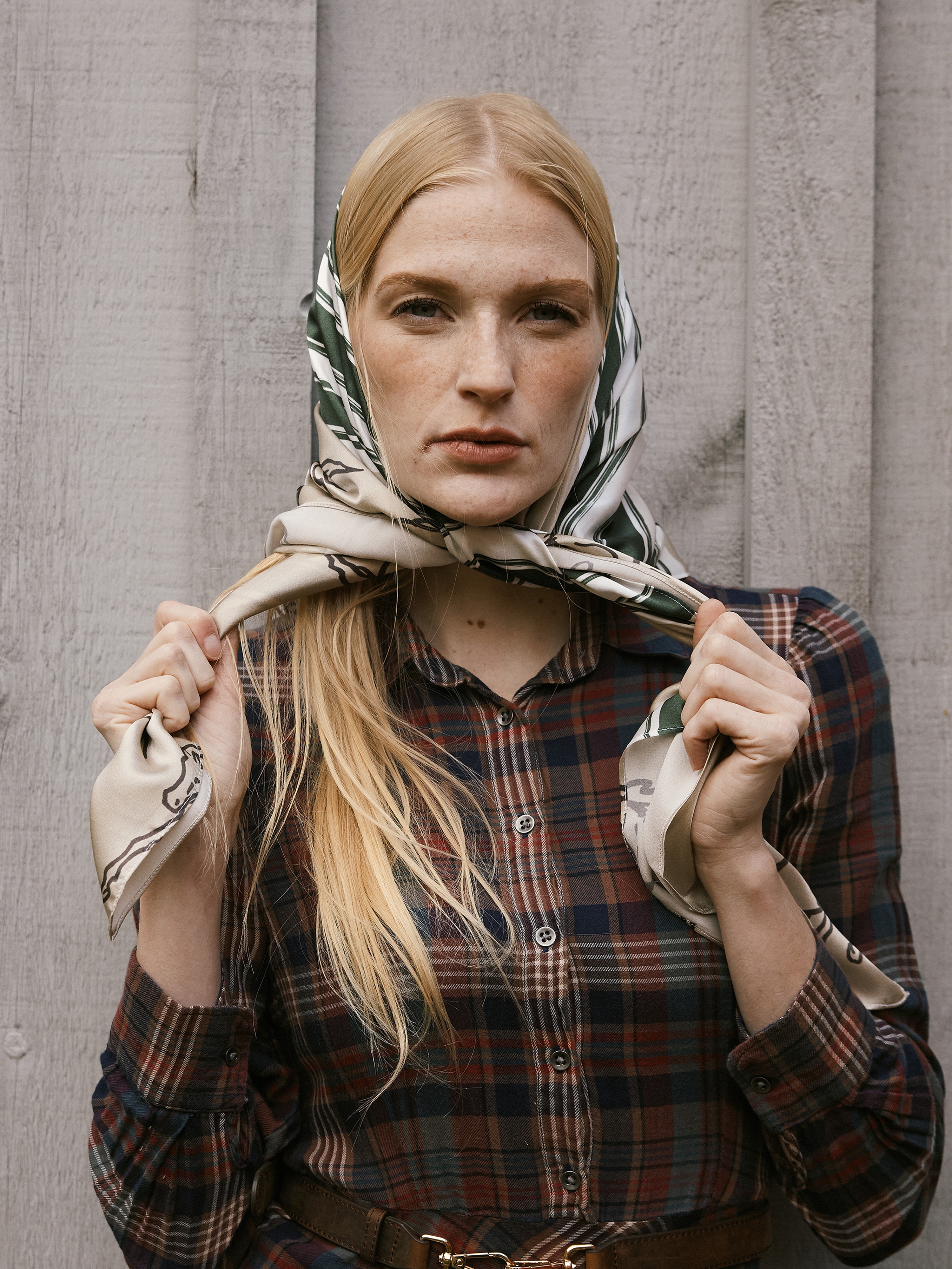 Woman wearing a patterned scarf and plaid shirt against a gray background
