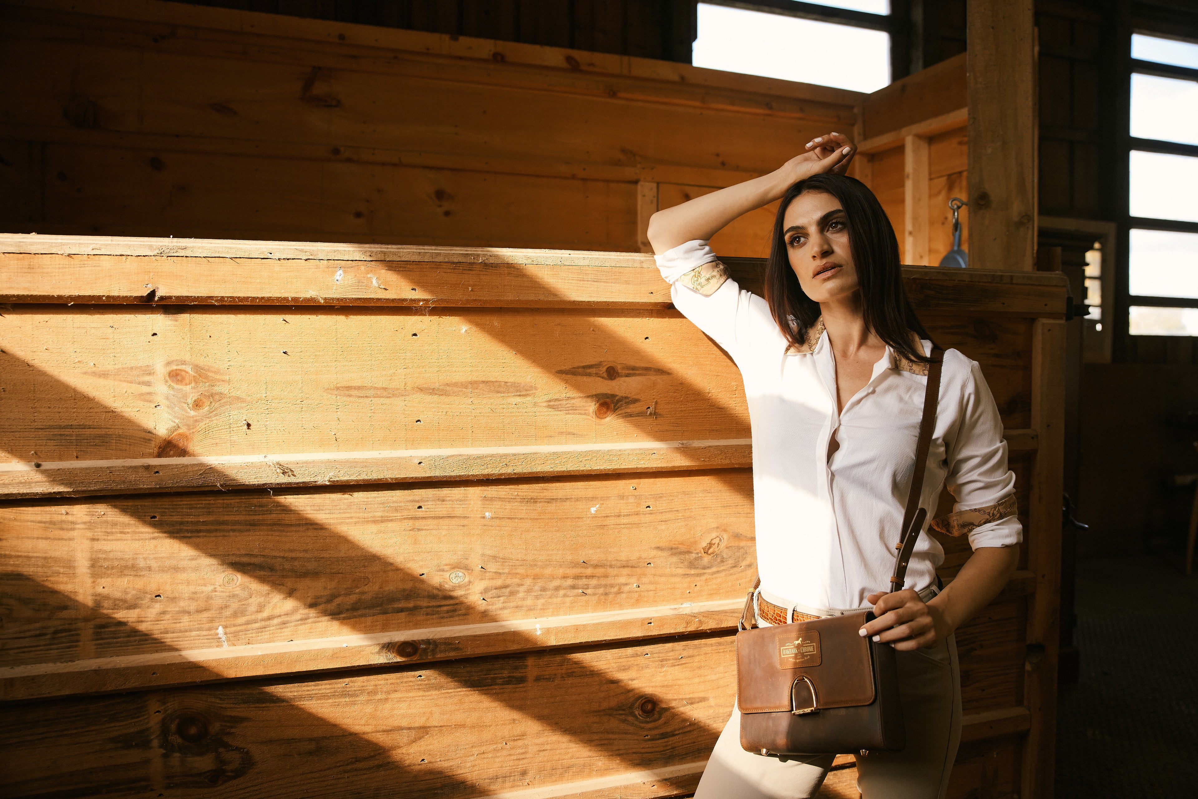 Woman standing in a sunlit wooden interior, holding a bag.
