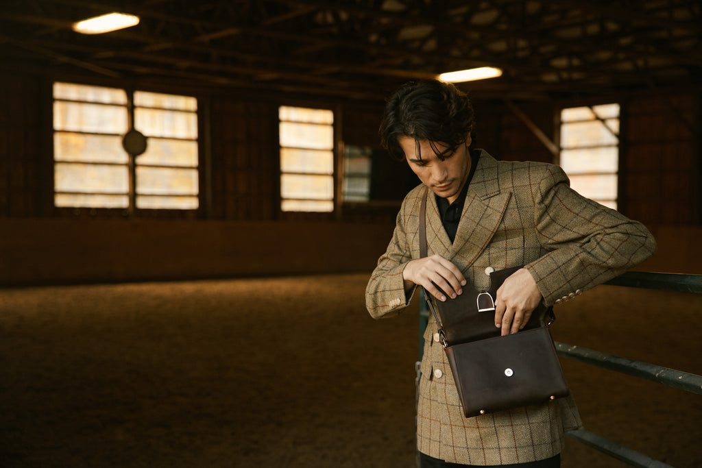 Man in a checkered coat holding a black bag in a dimly lit indoor setting