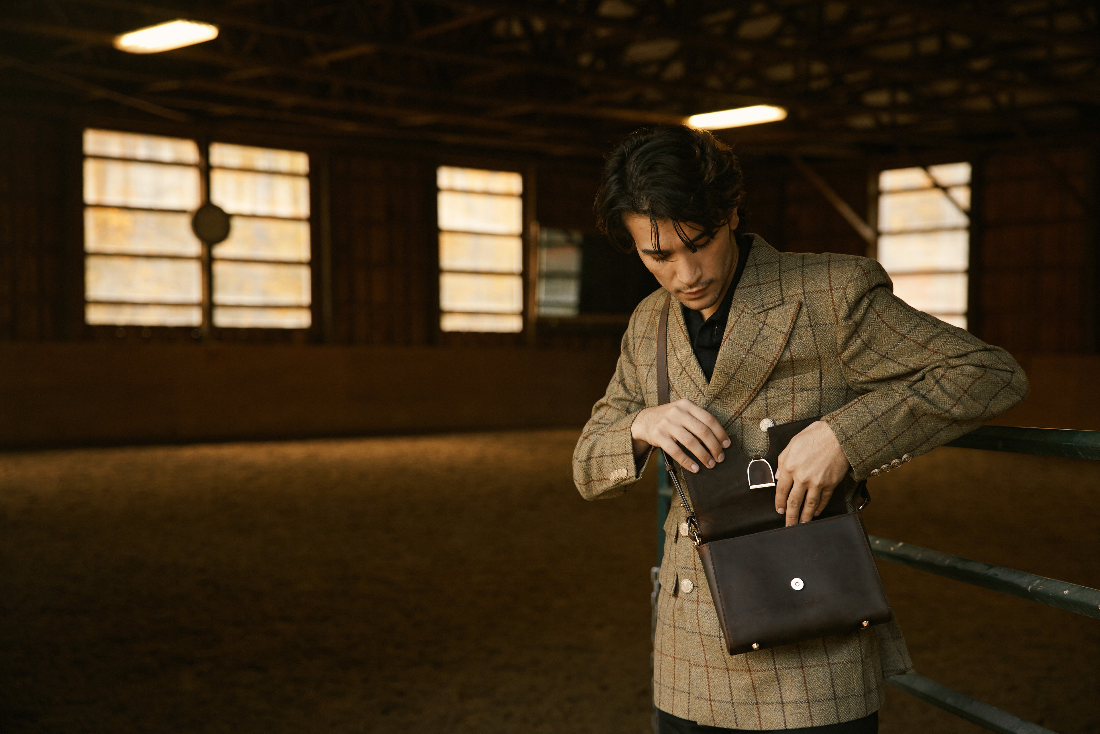 Man in a checkered coat holding a black bag in a dimly lit indoor setting