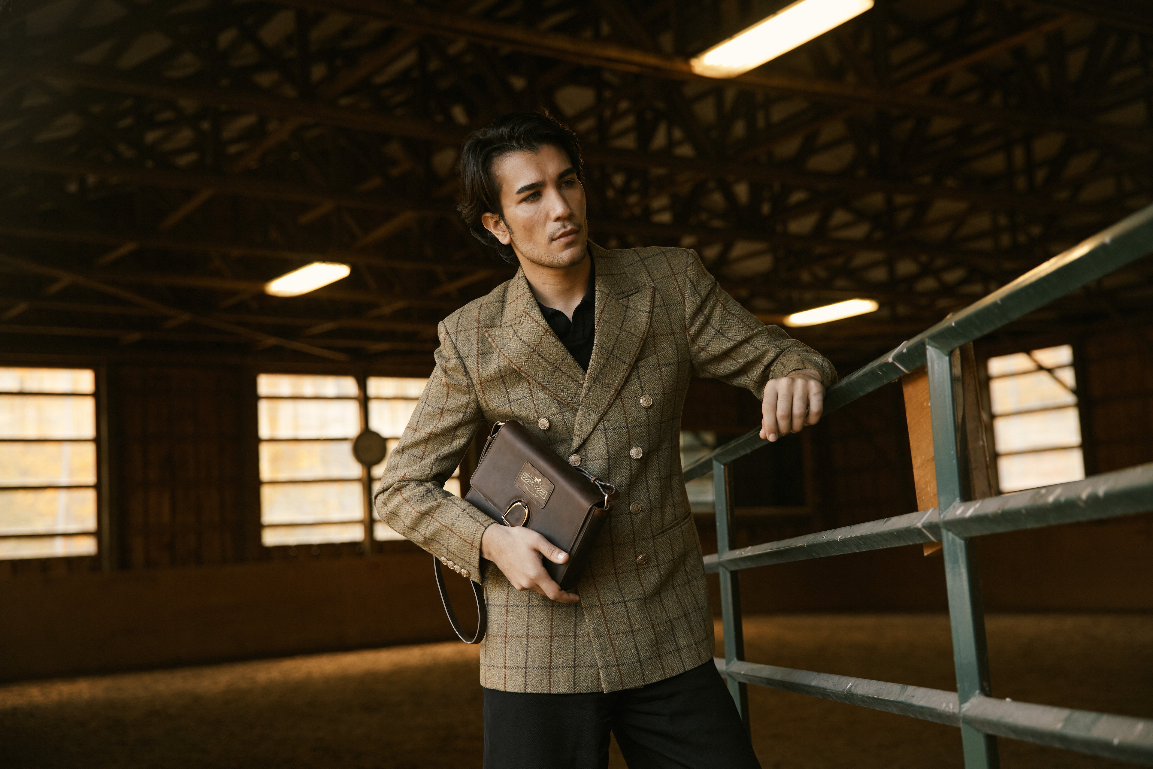 Man in a checkered suit holding a leather briefcase in an indoor setting.