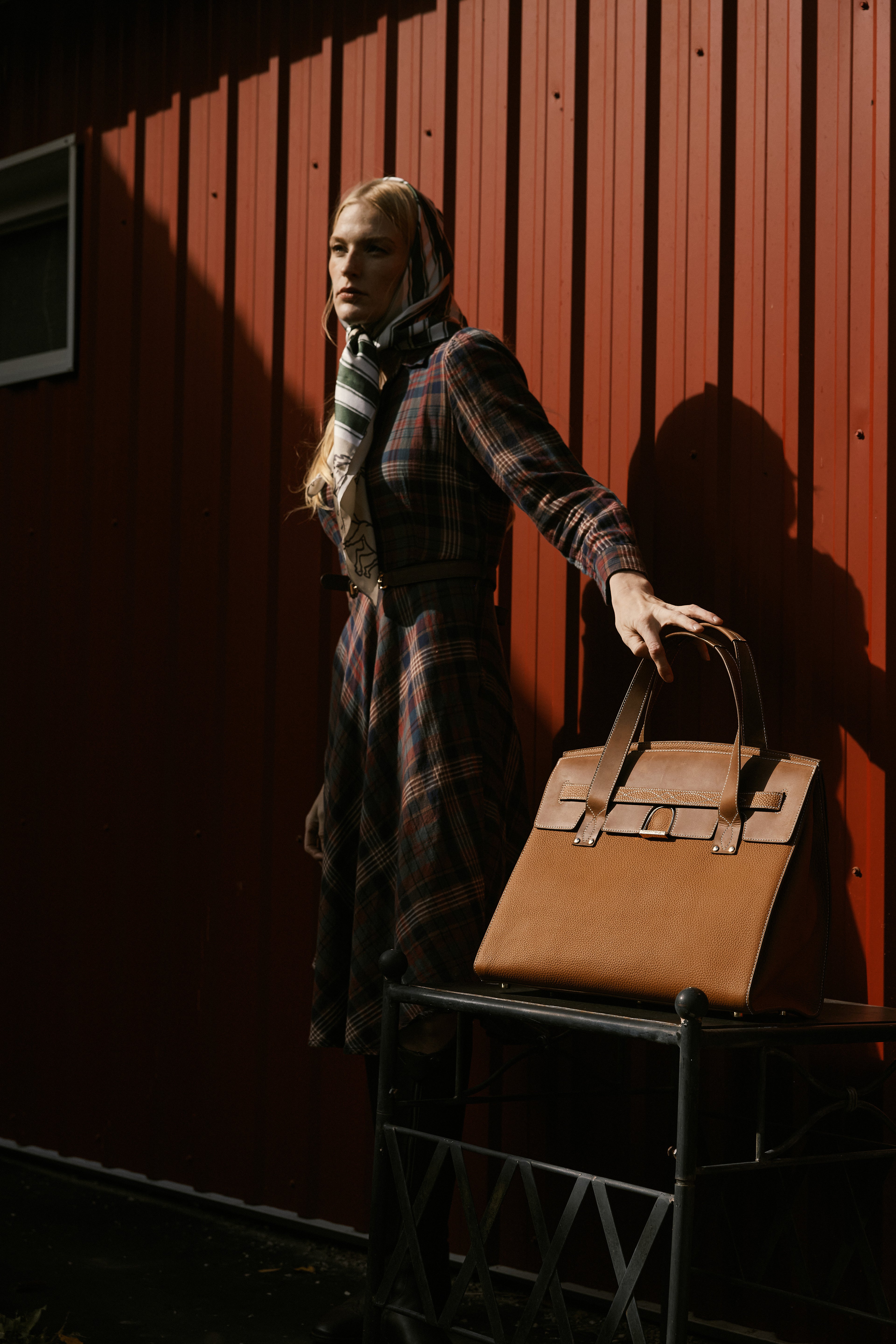 Woman holding a brown leather bag against a red wooden wall