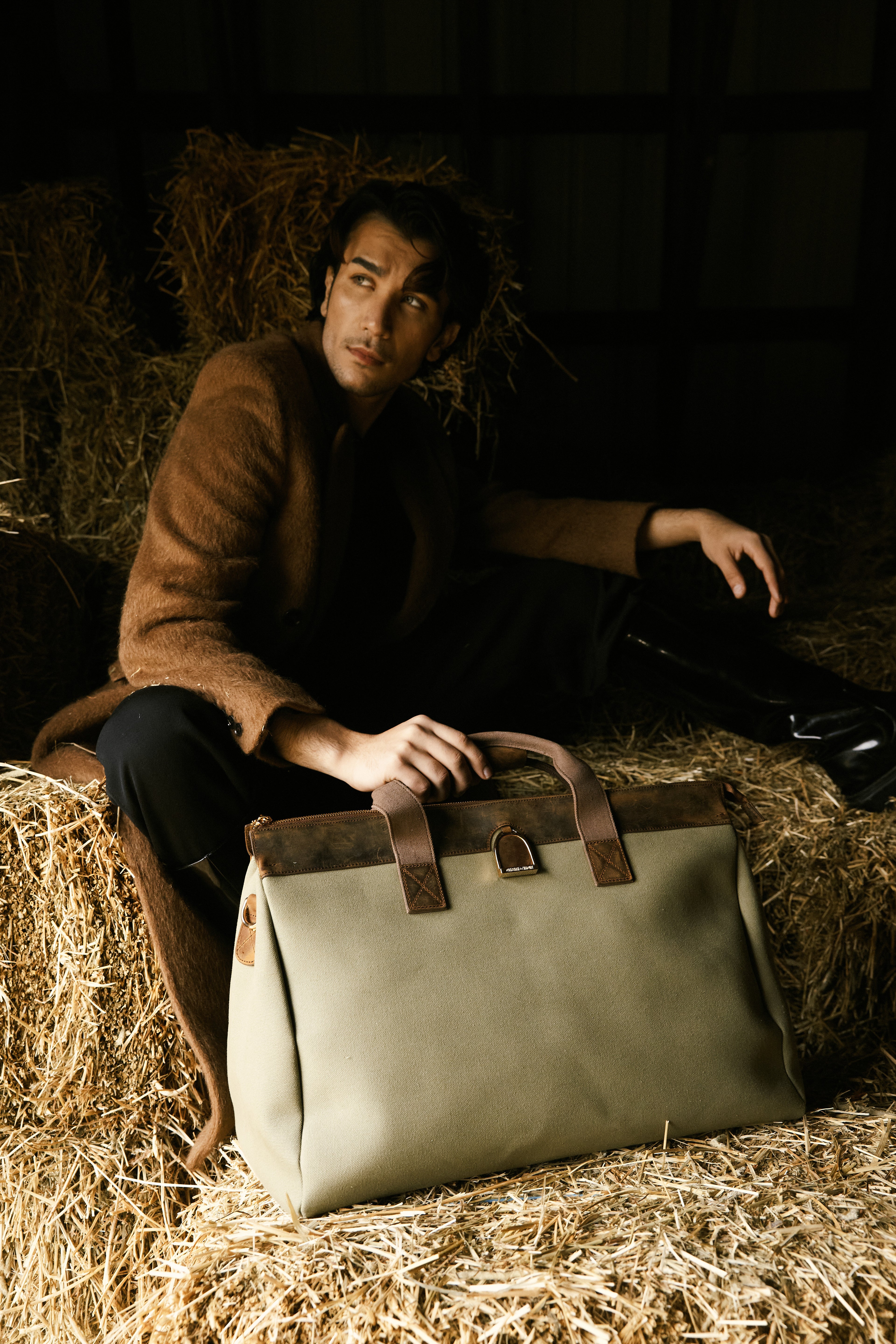 Man sitting on hay with a leather bag in a rustic setting